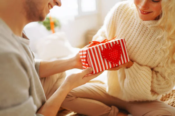 Young man giving present to his girlfriend at home. Beautiful young couple at home celebrating Valentine\'s Day. Romantic day.