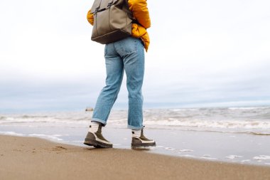 Çizmeli kadın bacaklarının yakın çekimi. Turistler deniz kenarında sahil boyunca yürürler. Macera, tatil konsepti. Etkin yaşam biçimi.