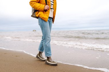 Çizmeli kadın bacaklarının yakın çekimi. Turistler deniz kenarında sahil boyunca yürürler. Macera, tatil konsepti. Etkin yaşam biçimi.