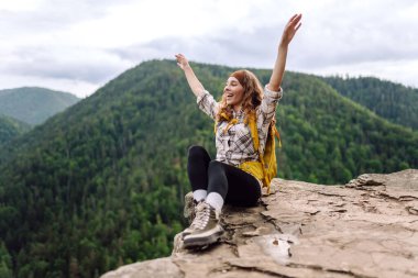 Sırt çantalı genç bir kadın dağın zirvesinde güzel bir dağa bakıyor. Yeşil tepeli, genç bir bayanla manzara. Yürüyüş. Doğa. Seyahat ve turizm.