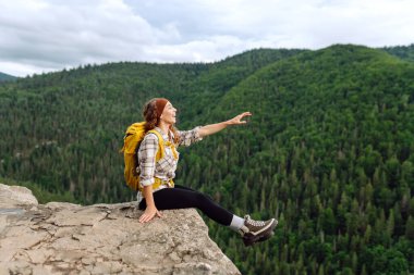 Sırt çantalı genç bir kadın dağın zirvesinde güzel bir dağa bakıyor. Yeşil tepeli, genç bir bayanla manzara. Yürüyüş. Doğa. Seyahat ve turizm.