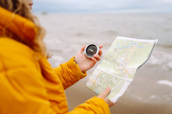 Traveler explorer young woman holding compass and a map in her hands on the beach near the sea. Adventure, vacation concept. Active lifestyle.