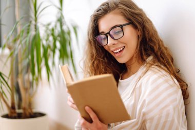 Genç bir kadın kitap okuyor, notlar yazıyor, evde ödev yapıyor. İş, blog yazma, serbest çalışma, eğitim kavramı. Dinlenme, rahatlama, rahatlama kavramı.