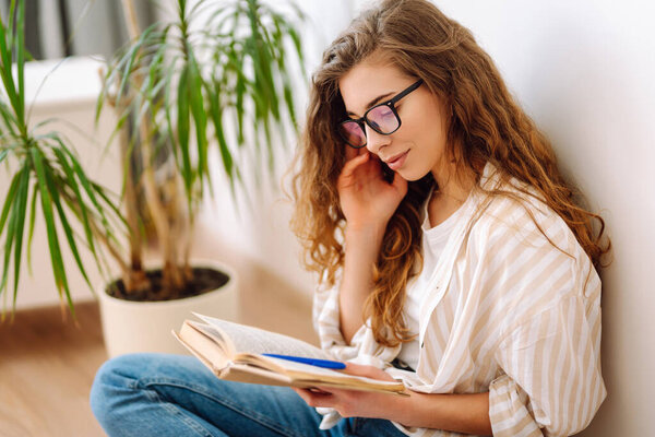 Young woman reading a book, writing notes, doing homework at home.  Business, blogging, freelance, education concept. Concept of rest, relaxation, comfort.