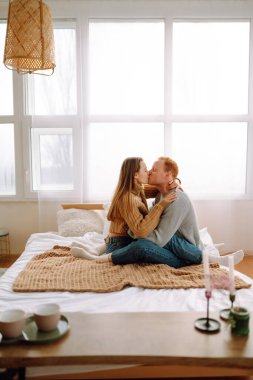 Mutlu genç çift evde birlikte yatakta dinleniyor. Yeni evliler, balayı seyahati. Öpüşüyor, sarılıyor ve eğleniyor..