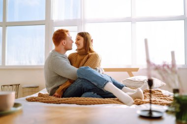 Mutlu genç çift evde birlikte yatakta dinleniyor. Yeni evliler, balayı seyahati. Öpüşüyor, sarılıyor ve eğleniyor..