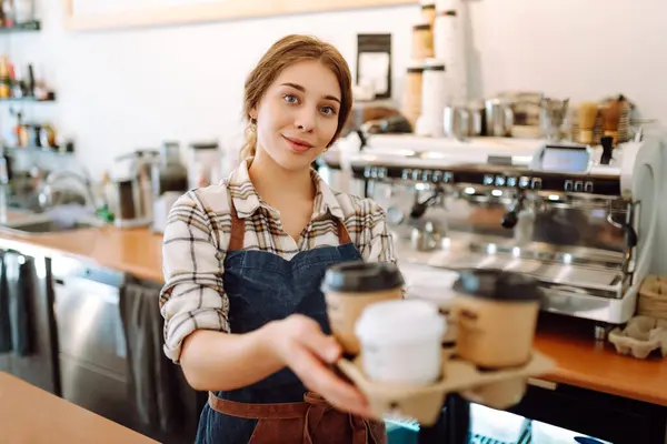 Takeaway food concept. Cheerful woman in an apron at the bar counter holds coffee glasses in a cafe. Food and drink.