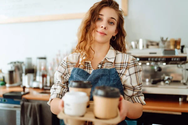 Takeaway food concept. Cheerful woman in an apron at the bar counter holds coffee glasses in a cafe. Food and drink.