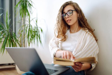 Genç kadın evde oturuyor, edebiyat ve laptop, bilgi ve eğitim kavramını kullanarak sınava hazırlanıyor..