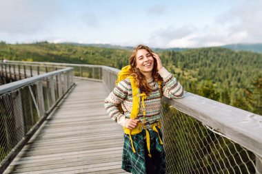 Genç bir kadın gezgin bir ormanın ortasında köprüden geçiyor. Seyahat ve aktif yaşam tarzı kavramı.