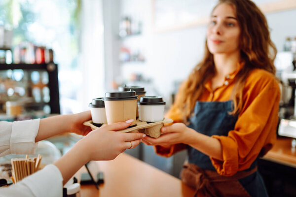 Takeaway food concept. A beautiful female barista gives to-go coffee to a client. Food and drink.