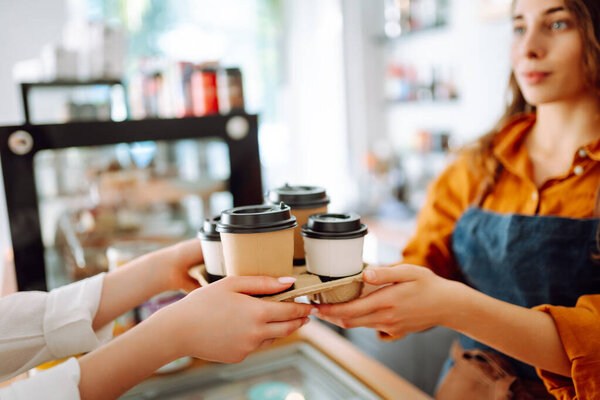 Takeaway food concept. A beautiful female barista gives to-go coffee to a client. Food and drink.