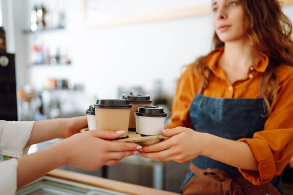 Takeaway food concept. A beautiful female barista gives to-go coffee to a client. Food and drink.