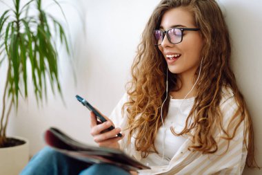 Cep telefonu modern teknolojisini kullanarak elinde akıllı telefon tutan mutlu bir kadın uzaktan çalışırken ya da öğrenirken cep telefonuna bakıyor, evde mesajlar yolluyor. İnternetten alışveriş, blog yazma, iletişim.