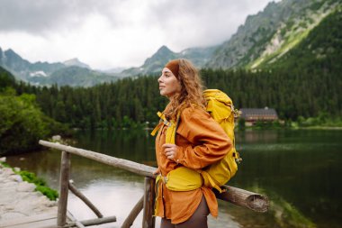 Sarı sırt çantalı mutlu kadın dağ manzarasının tadını çıkarıyor. Macera, seyahat, spor, aktif hayat.