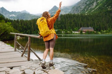 Sarı sırt çantalı mutlu kadın dağ manzarasının tadını çıkarıyor. Macera, seyahat, spor, aktif hayat.