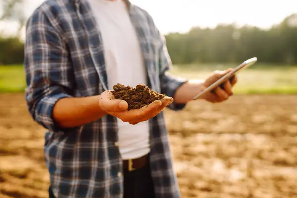 Farm hand holds black soil in her hands and checking with a digital tablet. Concept of agriculture, technology, business and ecology.