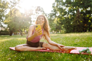 Genç bir kadın telefon ekranına el sallıyor, fitness eğitmeniyle online konferans yapıyor, video blogu kaydediyor. Güzel bir kadın eğitmen ya da takipçi. Spor, aktif yaşam, sağlıklı yaşam tarzı.