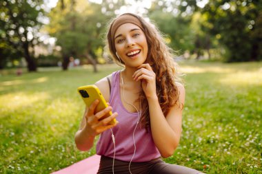 Genç bir kadın telefon ekranına el sallıyor, fitness eğitmeniyle online konferans yapıyor, video blogu kaydediyor. Güzel bir kadın eğitmen ya da takipçi. Spor, aktif yaşam, sağlıklı yaşam tarzı.