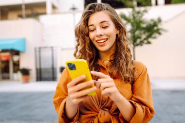 Sokakta yürüyen ve cep telefonu kullanan genç bir kadın. İş, teknoloji, blog, iletişim kavramı.