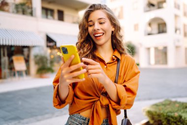 Sokakta yürüyen ve cep telefonu kullanan genç bir kadın. İş, teknoloji, blog, iletişim kavramı.