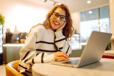 Kafede dizüstü bilgisayarlı genç bir kadın oturuyor. Kafede güzel bir üniversite öğrencisi. Eğitim, iş, blog veya serbest çalışma kavramı.