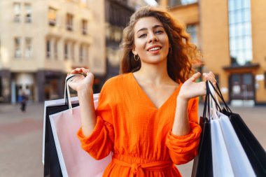 Alışveriş merkezinin yakınında alışveriş torbalarıyla yürüyen güzel bir kadın. Bahar stili. Tüketim, satın alma, alışveriş, yaşam tarzı, satış kavramı.