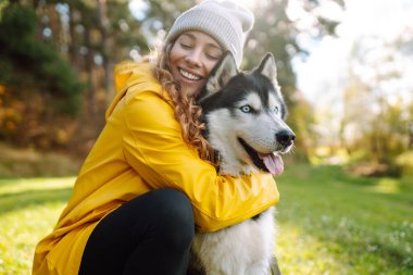 Sarı paltolu güzel genç bir kadın evcil köpeğiyle parkta yürüyor. Bir evcil hayvan sahibi köpeğiyle vakit geçirir. Eğlence anlayışı, eğlence.