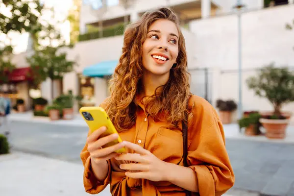 Sokakta yürüyen ve cep telefonu kullanan genç bir kadın. İş, teknoloji, blog, iletişim kavramı.