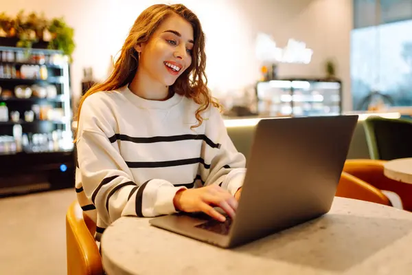 Young woman sitting on cafe with laptop. Beautiful college student on a cafe. Concept for education, business, blog or freelance.
