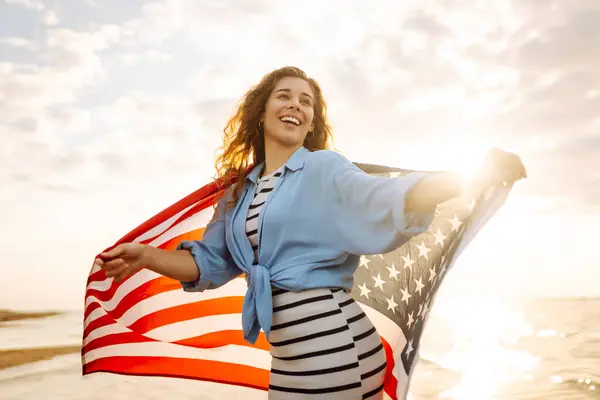 Happy woman holding United States of America flag and running  on the beach at sunset. Patriotic holiday. USA celebrate 4th of July. Independence Day concept