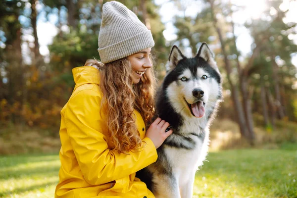 Sarı paltolu güzel genç bir kadın evcil köpeğiyle parkta yürüyor. Bir evcil hayvan sahibi köpeğiyle vakit geçirir. Eğlence anlayışı, eğlence.