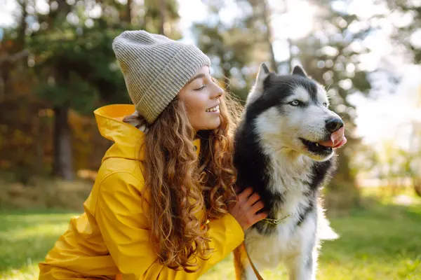 Sarı paltolu güzel genç bir kadın evcil köpeğiyle parkta yürüyor. Bir evcil hayvan sahibi köpeğiyle vakit geçirir. Eğlence anlayışı, eğlence.