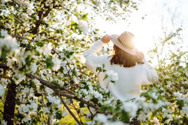 Çiçek açan bahar bahçesinde kokunun tadını çıkaran genç bir kadın. Gençlik, aşk, moda, turizm ve yaşam tarzı kavramı