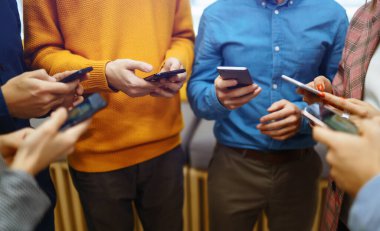 Cep telefonu kullanan bir grup genç. Dijital cihazlar kullanarak modern bir ofiste yan yana oturan mutlu colegiolar. Bilgi teknolojisi aygıtı, eğitim, sosyal ağ ile modern yaşam tarzı.