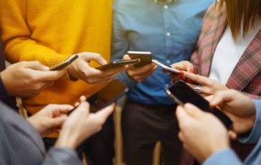 Cep telefonu kullanan bir grup genç. Dijital cihazlar kullanarak modern bir ofiste yan yana oturan mutlu colegiolar. Bilgi teknolojisi aygıtı, eğitim, sosyal ağ ile modern yaşam tarzı.