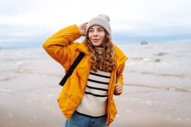 Sarı ceketli ve deniz kenarında poz veren mutlu bir turist. Seyahat, yaşam tarzı, macera.