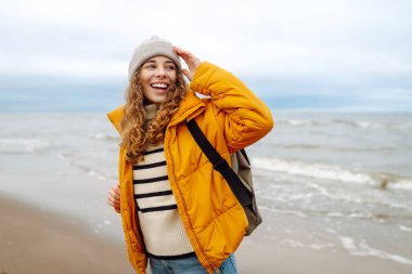 Sarı ceketli ve deniz kenarında poz veren mutlu bir turist. Seyahat, yaşam tarzı, macera.