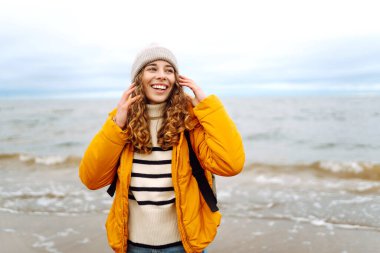 Sarı ceketli ve deniz kenarında poz veren mutlu bir turist. Seyahat, yaşam tarzı, macera.