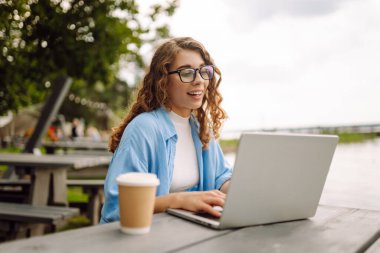 İnternette dizüstü bilgisayar kullanarak çalışan ve göle bakan doğal manzaranın tadını çıkaran güzel bir kadının portresi. Eğitim, iş, blog veya serbest çalışma kavramı.