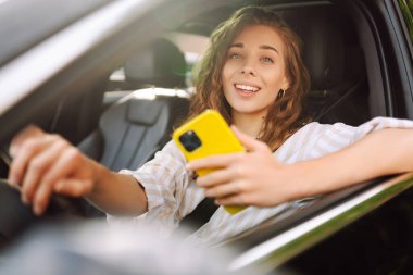Telefonlu bir kadın sürücü. Araba kullanırken akıllı telefondan mesaj atan bir kadın. E-posta sohbetlerini kontrol edip, haberleri okuyorum. Seyahat, teknoloji, internet kavramı. 