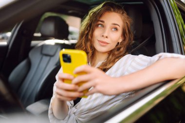 Telefonlu bir kadın sürücü. Araba kullanırken akıllı telefondan mesaj atan bir kadın. E-posta sohbetlerini kontrol edip, haberleri okuyorum. Seyahat, teknoloji, internet kavramı. 