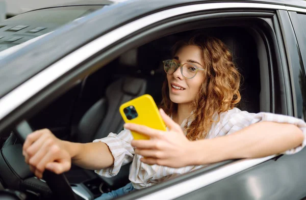 A woman driver  with phone. Woman texting on smartphone while driving car. Checking email chats and reading news. Concept of travel, technology, internet.