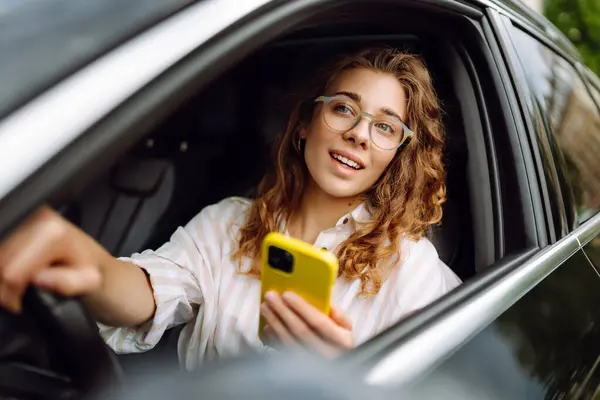 A woman driver  with phone. Woman texting on smartphone while driving car. Checking email chats and reading news. Concept of travel, technology, internet.