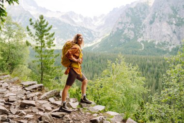 Sırt çantalı yürüyüş yapan genç bir kadın. Doğa yürüyüşü. Güneşli bir manzara. Genç bir gezgin dağ patikaları boyunca seyahat eder. Macera, seyahat konsepti.
