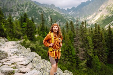 Sırt çantalı yürüyüş yapan genç bir kadın. Doğa yürüyüşü. Güneşli bir manzara. Genç bir gezgin dağ patikaları boyunca seyahat eder. Macera, seyahat konsepti.