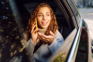 Güzel genç bir kadın arabanın arka koltuğunda otururken akıllı telefon kullanır. Arabada seyahat eden bir kadın telefonda konuşuyor. İnternet ve sosyal medya.