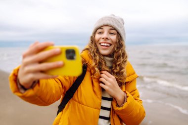 Genç bir kadın sahilde selfie çekiyor. Seyahat, yaşam tarzı, macera. Günlük tutma.