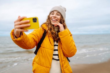 Genç bir kadın sahilde selfie çekiyor. Seyahat, yaşam tarzı, macera. Günlük tutma.
