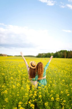 Gülümseyen kadın turistler çiçek tarlasında yürürler, sarı çiçeklere dokunurlar. Doğa, tatil, rahatlama ve yaşam tarzı. Yaz manzarası.